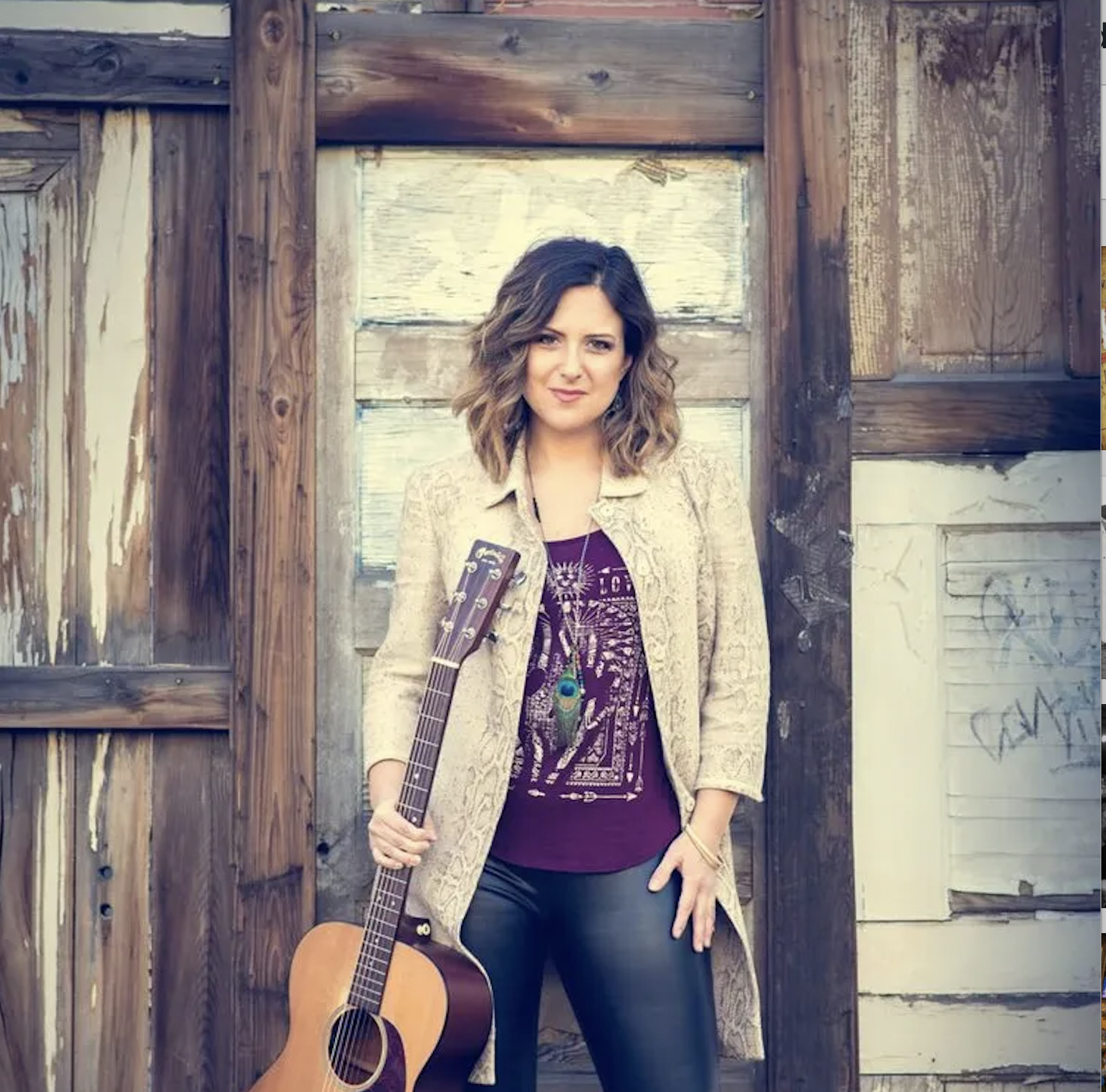 A blonde woman holding a guitar in right hand