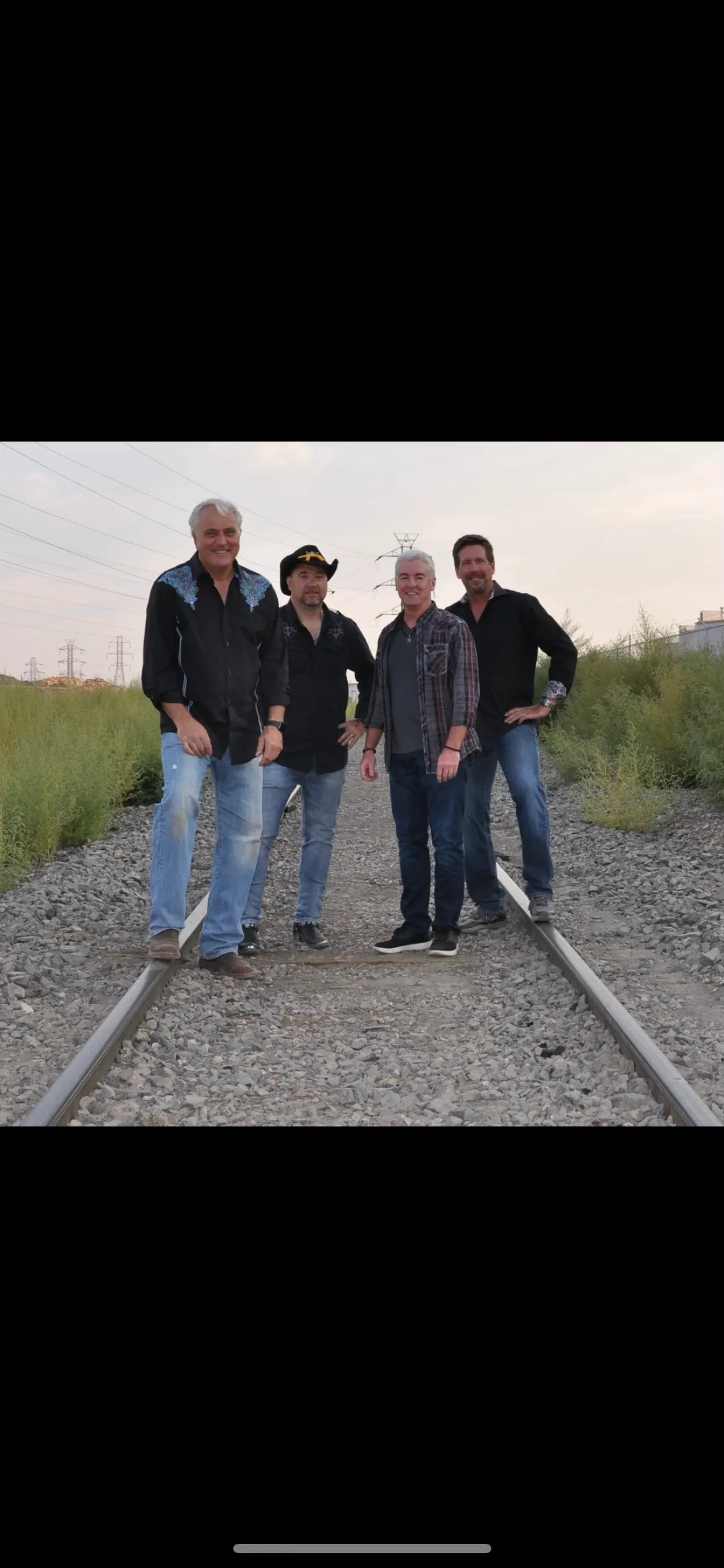 Four guys posing in jeans on railroad tracks